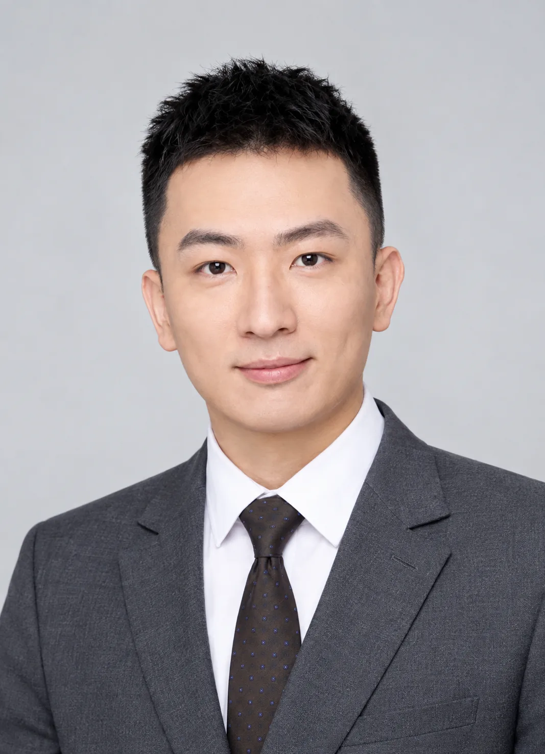 Portrait of Geng Wang wearing a charcoal suit against a light gray background